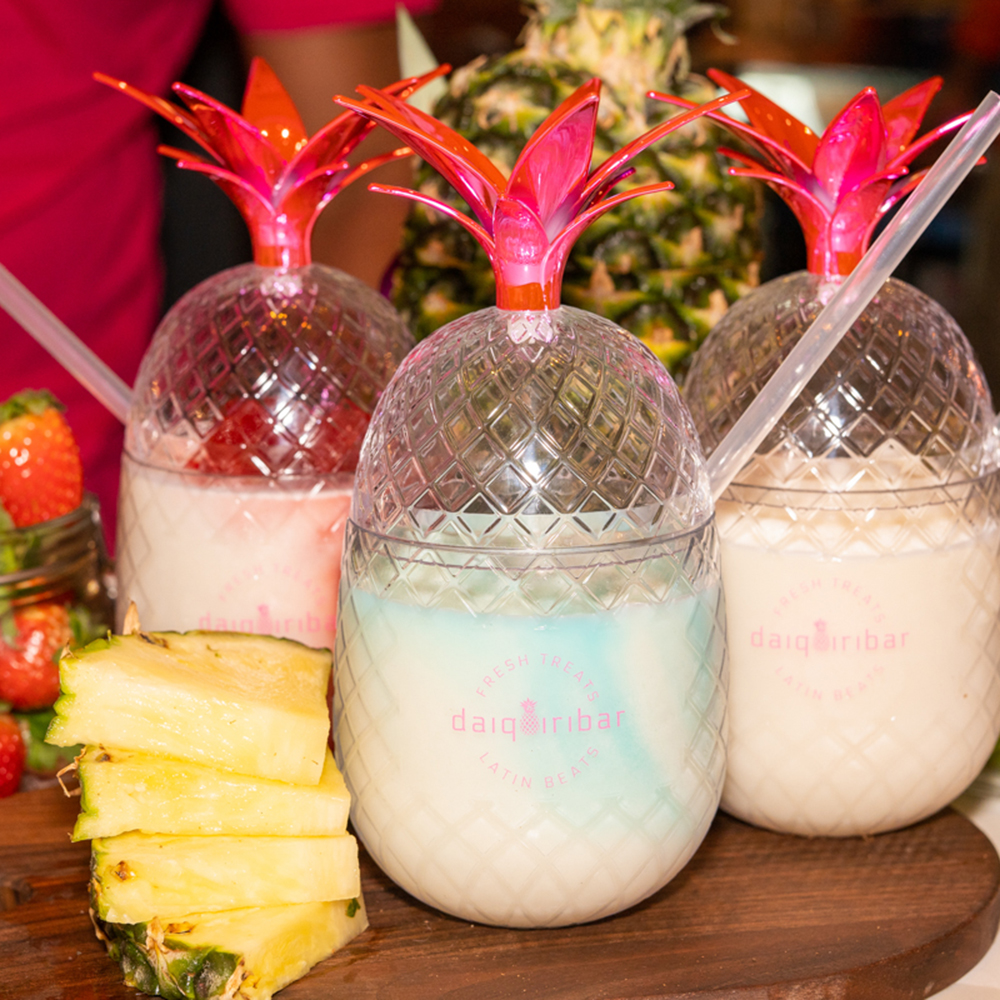 3 pineapple vessels with daiquiris, fresh pineapples sliced and strawberries on the side