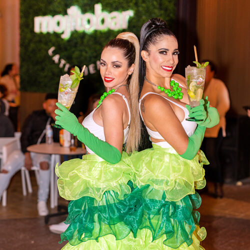 two dancers in green and yellow outfits, holding mojitos